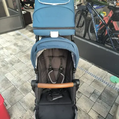 Mockingbird double stroller in teal and black, featuring a brown leatherette bumper bar and adjustable canopies.