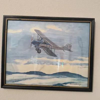 Framed aviation print by Charles H. Hubbell depicting a vintage biplane in flight, housed in a black frame with gold inner trim.