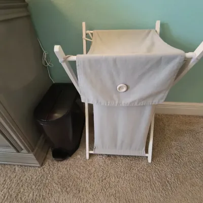 Folding wooden laundry hamper with a removable light gray fabric liner featuring a decorative button closure, shown next to a black...