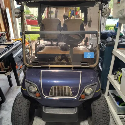 Dark blue custom golf cart featuring a front grille, headlights, a folding windshield, and a matching blue canopy top.