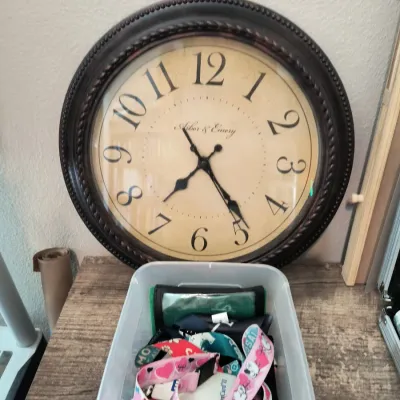 Arbor & Emery large round wall clock with a dark, beaded-edge frame and an aged parchment-style face, shown behind a plastic bin of...