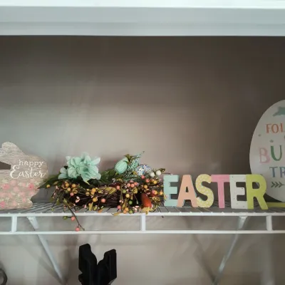 Assorted Easter decorations, including a wooden bunny sign, a small floral nest arrangement, colorful block letters spelling...