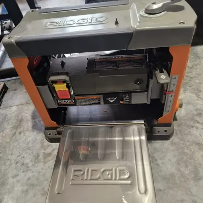 Ridgid portable thickness planer with orange and grey housing, featuring a fold-down stainless steel feed table and top-mounted...