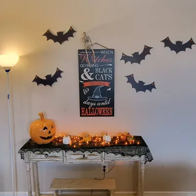 Shabby chic distressed white console table decorated with Halloween decor, including a countdown sign, bat wall cutouts, a ceramic...