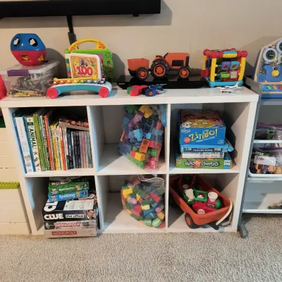 White six-cube organizer shelf filled with various children's toys, books, board games, and building blocks.