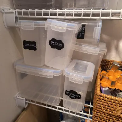 Assorted clear plastic food storage containers with locking lids and chalkboard labels, shown on a wire pantry shelf.