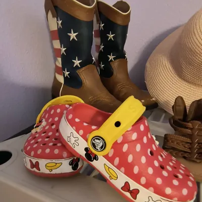 Pair of children's Disney Minnie Mouse Crocs with red and white polka dots, shown alongside a pair of patriotic American flag cowboy...