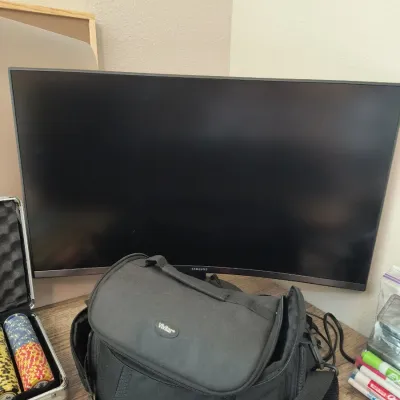 Samsung curved computer monitor paired with a black Vivitar camera bag and a partial view of a poker chip set.