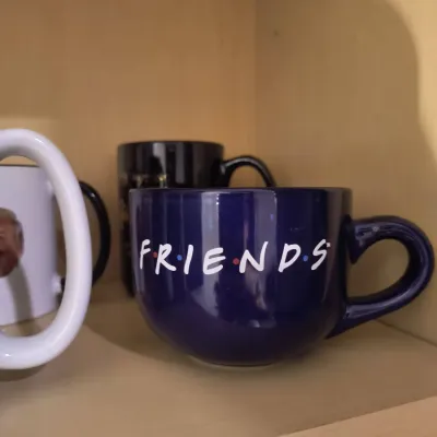 Dark blue ceramic Friends television show mug, displayed on a shelf alongside other mugs.