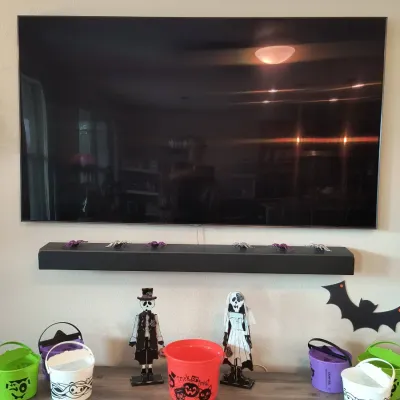 Wall-mounted flat-screen television and matching soundbar, displayed above a collection of Halloween decorations including trick-or-treat...