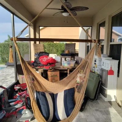 Hanging woven rope hammock chair with a wooden spreader bar and a blue and white striped accent pillow, shown suspended on a screened-in...