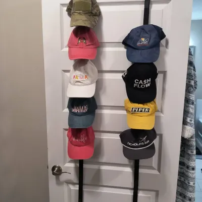 Collection of assorted baseball caps displayed on two over-the-door hanging organizers, featuring various colors, logos, and text designs.