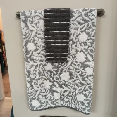 Grey and white floral patterned bath towel paired with a dark grey striped hand towel, hanging on a metal towel bar.