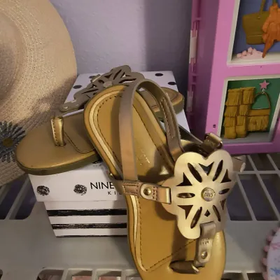 Nine West Kids gold metallic thong sandals with decorative cutout flower details, displayed on their original box.