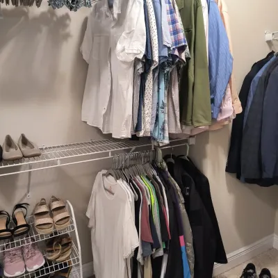 Assorted men's clothing including button-down shirts, t-shirts, jackets, and shoes displayed on closet racks and shelves.