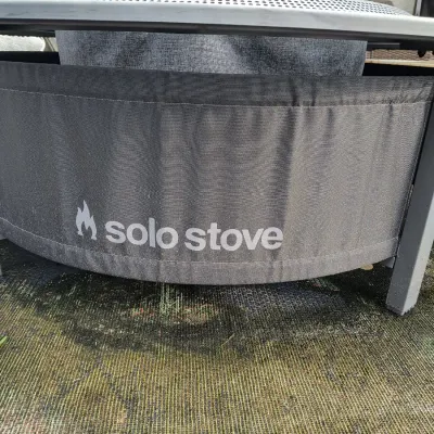 Solo Stove fire pit with a protective fabric surround and a metal lid, showing light outdoor wear.