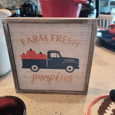 Rustic wooden block sign featuring a vintage blue truck carrying pumpkins and the text "Farm Fresh pumpkins."