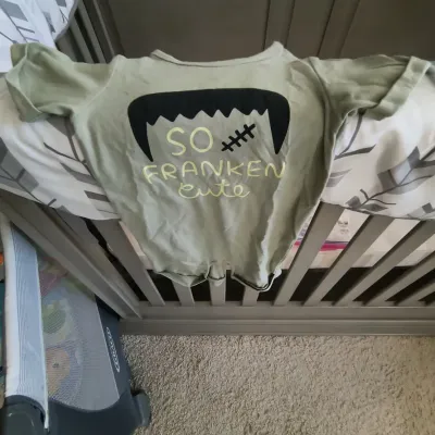 Sage green infant bodysuit featuring a Frankenstein graphic and the phrase "So Franken Cute" draped over a wooden crib.
