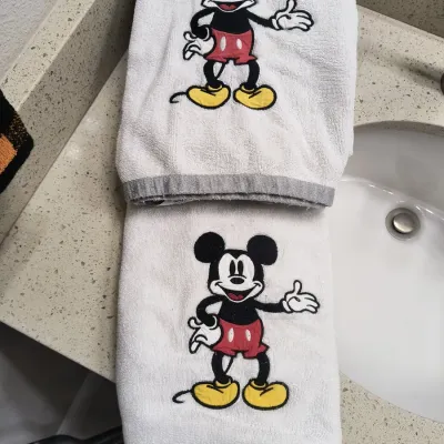 Pair of white Disney Mickey Mouse hand towels with embroidered character details and grey trim.