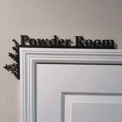 Black metal "Powder Room" door topper sign featuring a decorative leaf and branch design on the left corner.