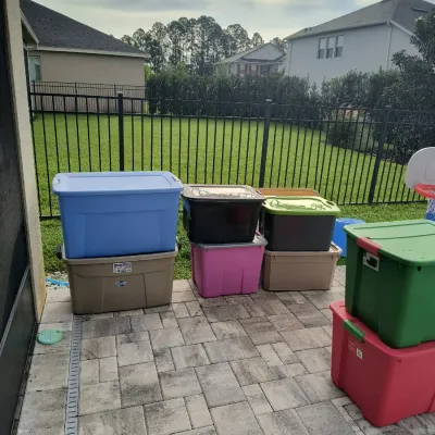 Assorted plastic storage bins in various sizes and colors, including blue, green, pink, and tan, stacked on a paved patio.