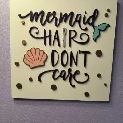 Square wooden wall art featuring the phrase 'mermaid hair don't care' in raised lettering, accented with a seashell, a...