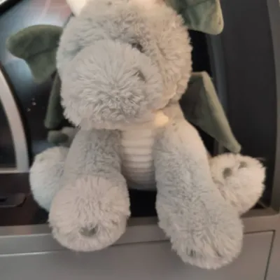 Plush grey dragon stuffed animal with green wings and white horns, in gently used condition.