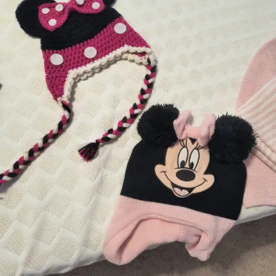 Two Minnie Mouse themed children's winter hats, including a hand-crocheted earflap hat with braided tassels and a knit fleece-lined...