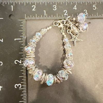 chunky silver-toned charm bracelet featuring large faceted crystal beads and playful ocean-themed dangles like a starfish and a sea turtle.