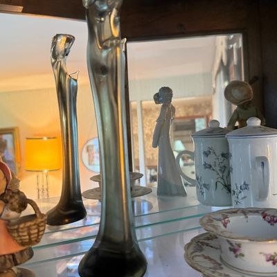 Art Nouveau style frosted glass bud vases shaped as stylized female figures, displayed alongside porcelain teacups and figurines on a...