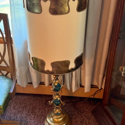 Vintage mid-century table lamp featuring an ornate gold-finished metal base with teal accents and a tall, cylindrical drum shade with...