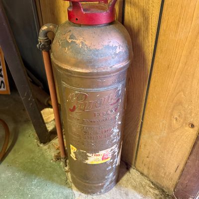 Vintage Pyrene copper and brass foam fire extinguisher with a red painted handle, showing a weathered patina and original labeling.