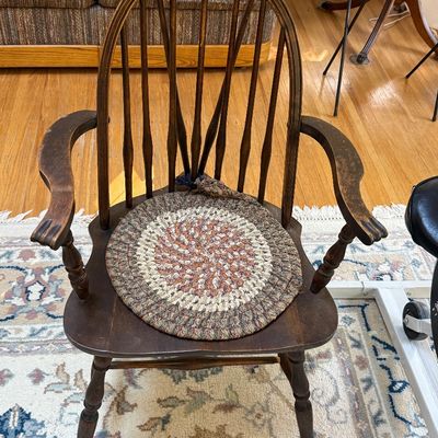 Vintage dark-stained wood Windsor-style armchair featuring a high spindle back, curved armrests, and a round braided chair pad.