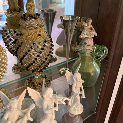Assorted vintage collectibles displayed in a curio cabinet, including white porcelain angel figurines, a green glass pitcher, silver-tone...