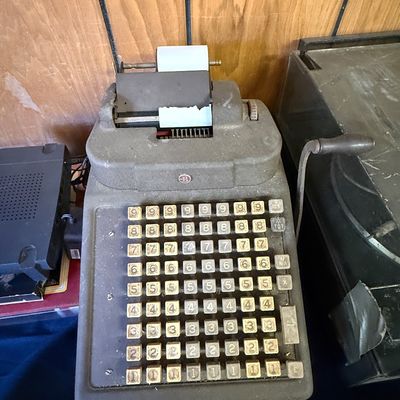Vintage Burroughs mechanical adding machine with a textured grey metal housing and a full keyboard of numbered keys, showing some dust...