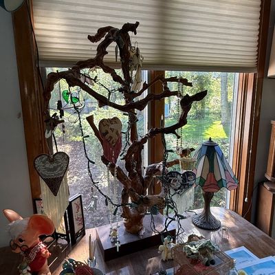 Eclectic tabletop display featuring a natural wood branch jewelry tree adorned with hanging ornaments, alongside a small Tiffany-style...