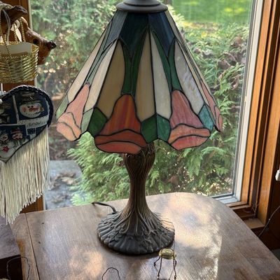 Tiffany-style stained glass table lamp featuring a floral tulip motif in pink, green, and cream panels on an ornate cast metal base.