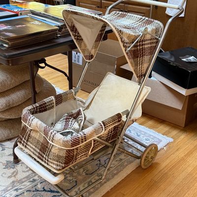 Vintage Welsh baby stroller featuring a brown and beige plaid fabric canopy and seat, with a chrome frame and white plastic handle, circa...