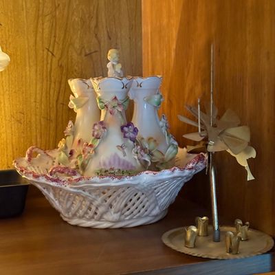 Vintage porcelain tulipiere vase with applied floral details and a reticulated basket base, shown alongside a small brass angel chimes...