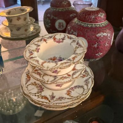 Vintage porcelain tableware collection, featuring floral-patterned soup bowls with matching saucers alongside two red Chinese ginger jars...
