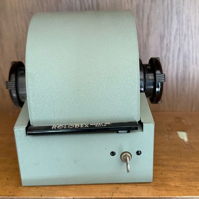 Vintage Rolodex model 2254D rotary card file in a sage green metal housing, featuring a lockable roll-top cover with key included.