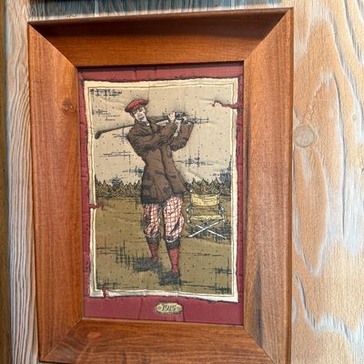 Framed fabric art piece depicting a vintage golfer in 1915 attire, set in a wide wooden frame.