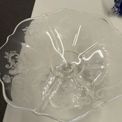 Vintage clear glass pedestal cake stand featuring an etched floral and scroll pattern with a ruffled rim.