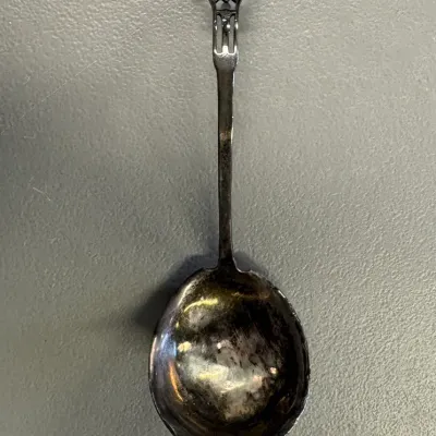 Antique sterling silver bonbon spoon featuring a round, shallow bowl and an ornate, openwork handle with a monogrammed finial.
