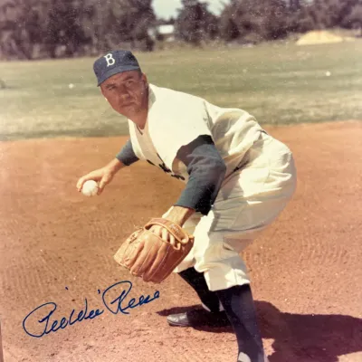 Autographed color photograph of Brooklyn Dodgers shortstop Pee Wee Reese in a fielding pose, signed in blue ink.