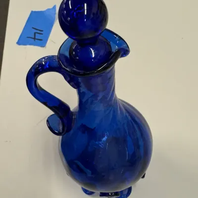 Vintage cobalt blue glass decanter with a matching ball stopper, featuring a curved handle and footed base.