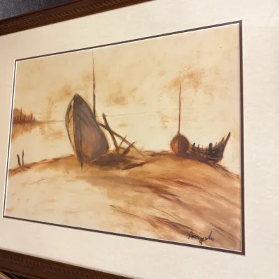 Framed sepia-toned watercolor painting depicting beached boats on a shoreline, signed by the artist in the lower right corner.