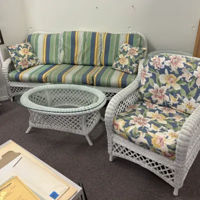 White wicker living room set including a sofa with striped cushions, a matching armchair with floral cushions, and an oval glass-top...