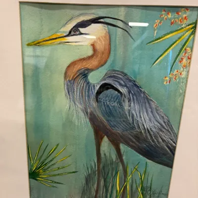 Framed watercolor painting of a great blue heron standing in a marsh, signed by the artist in the lower right corner.