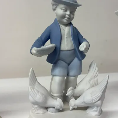 Vintage porcelain figurine depicting a young boy feeding chickens, finished in a matte blue and white glaze.